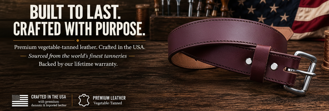 A premium vegetable-tanned leather belt in a deep reddish-brown color, displayed on a rustic wooden surface next to a small branded leather patch and an American flag. The background features dark wood, cutlery, and a warm, patriotic American theme.